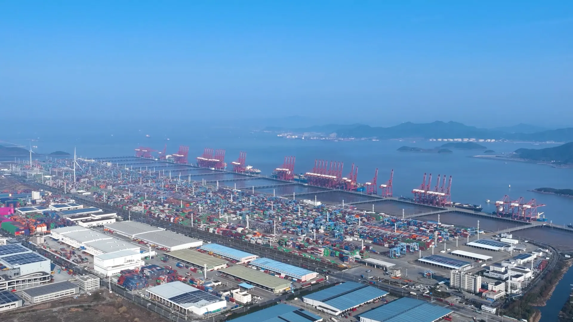 Daytime aerial of the container terminal and bay, quay cranes lined up along the berths