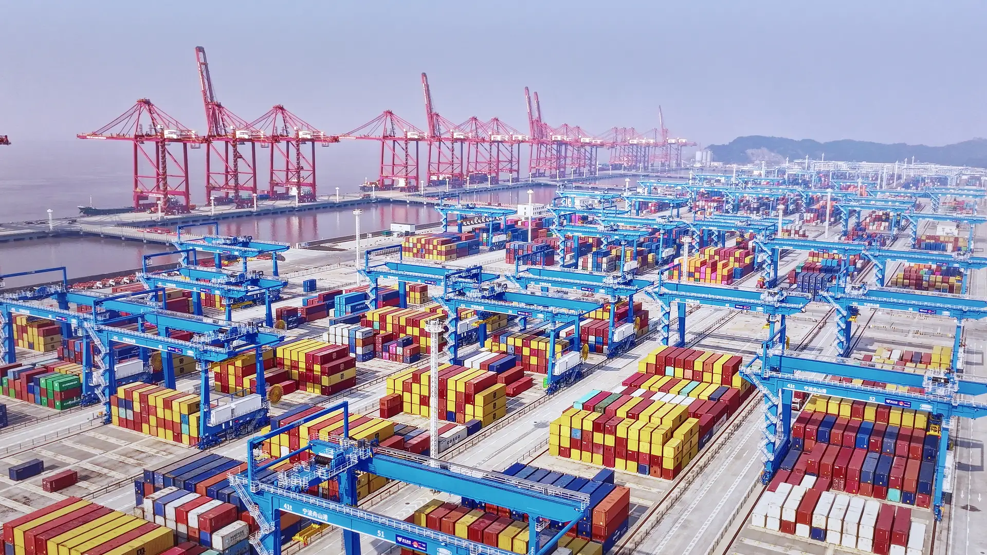 Aerial view of an automated yard, rows of blue rail-mounted gantry cranes spanning the container blocks